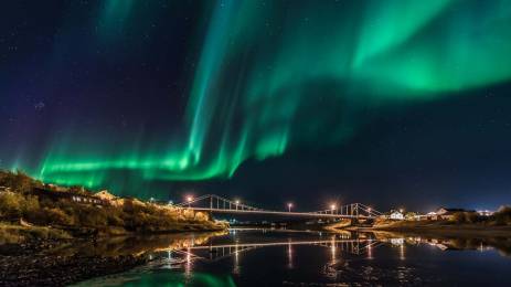 Nordlys over opplyst bro ved fjorden