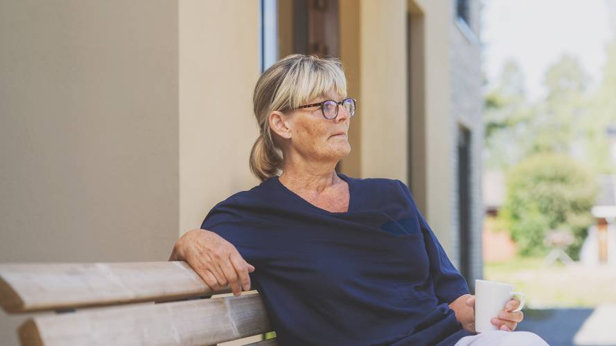 sykepleier som sitter ute på en benk med kaffekopp i hånden