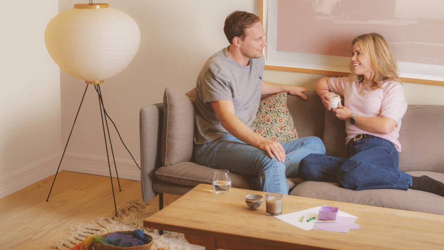 Smilende ung mann og kvinne med kaffekopp snakker i sofaen