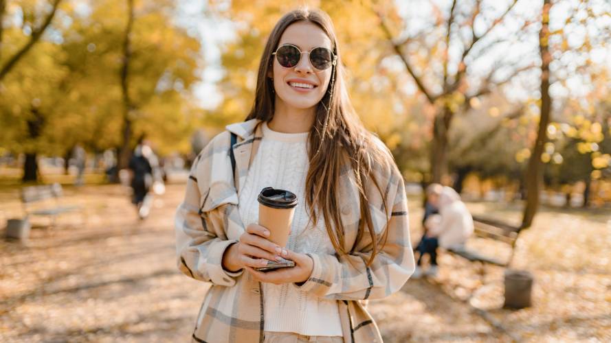 Dame med solbriller og kaffekopp som smiler