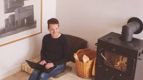 Voksen mann med laptop sitter ved en peisovn og tenker