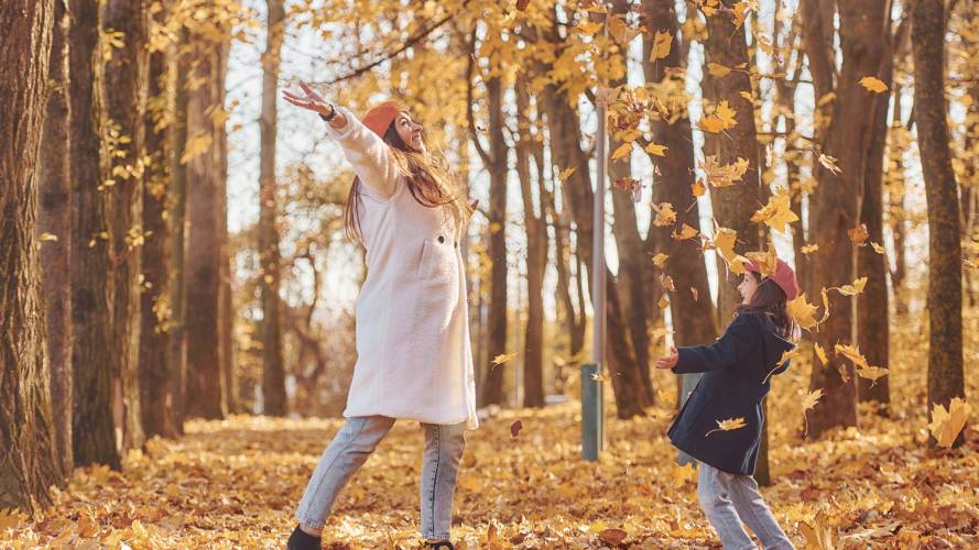 Dame og jente som kaster gult løv opp i luften 
