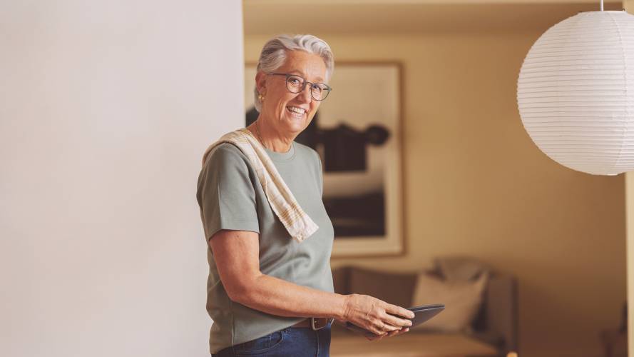 Voksen smilende kvinne på kjøkkenet med tallerkener i hendene