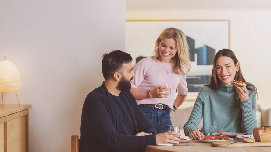 Tre unge voksne har lunsj sammen ved et dekket kjøkkenbord