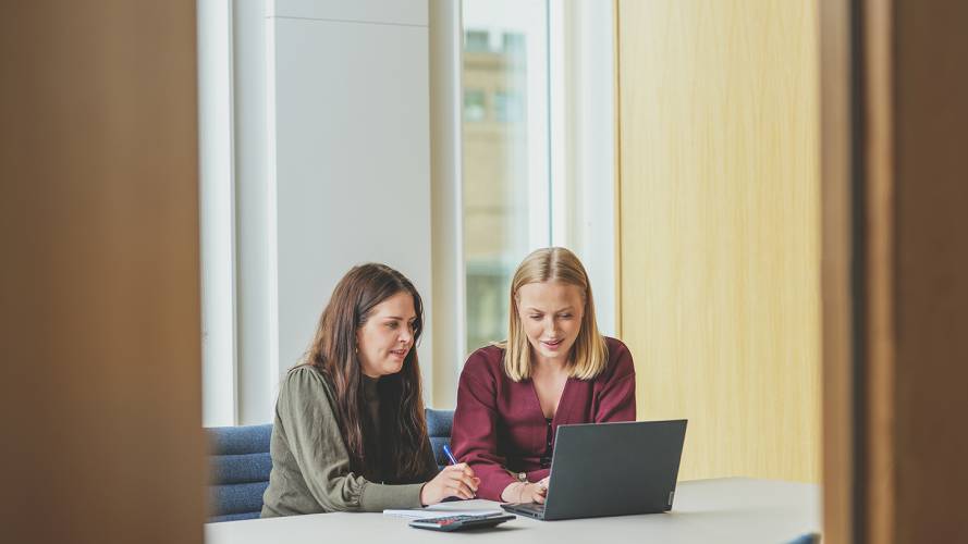 To damer som sitter sammen og ser på en pc og noterer