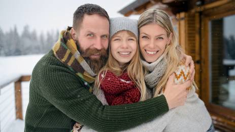 Familie på tre som klemmer hverandre ute på vinteren