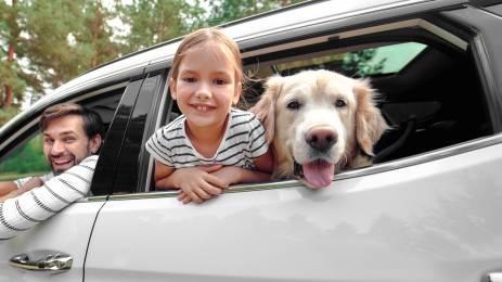 Far, datter og hund som smiler ut av vinduet i en bil