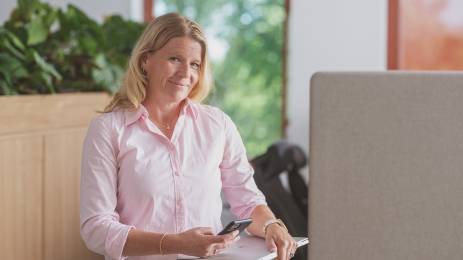 Dame med pc og mobil i hendene som smiler