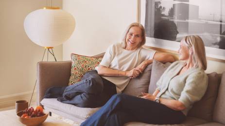 To voksne venninner sitter i en sofa og smiler